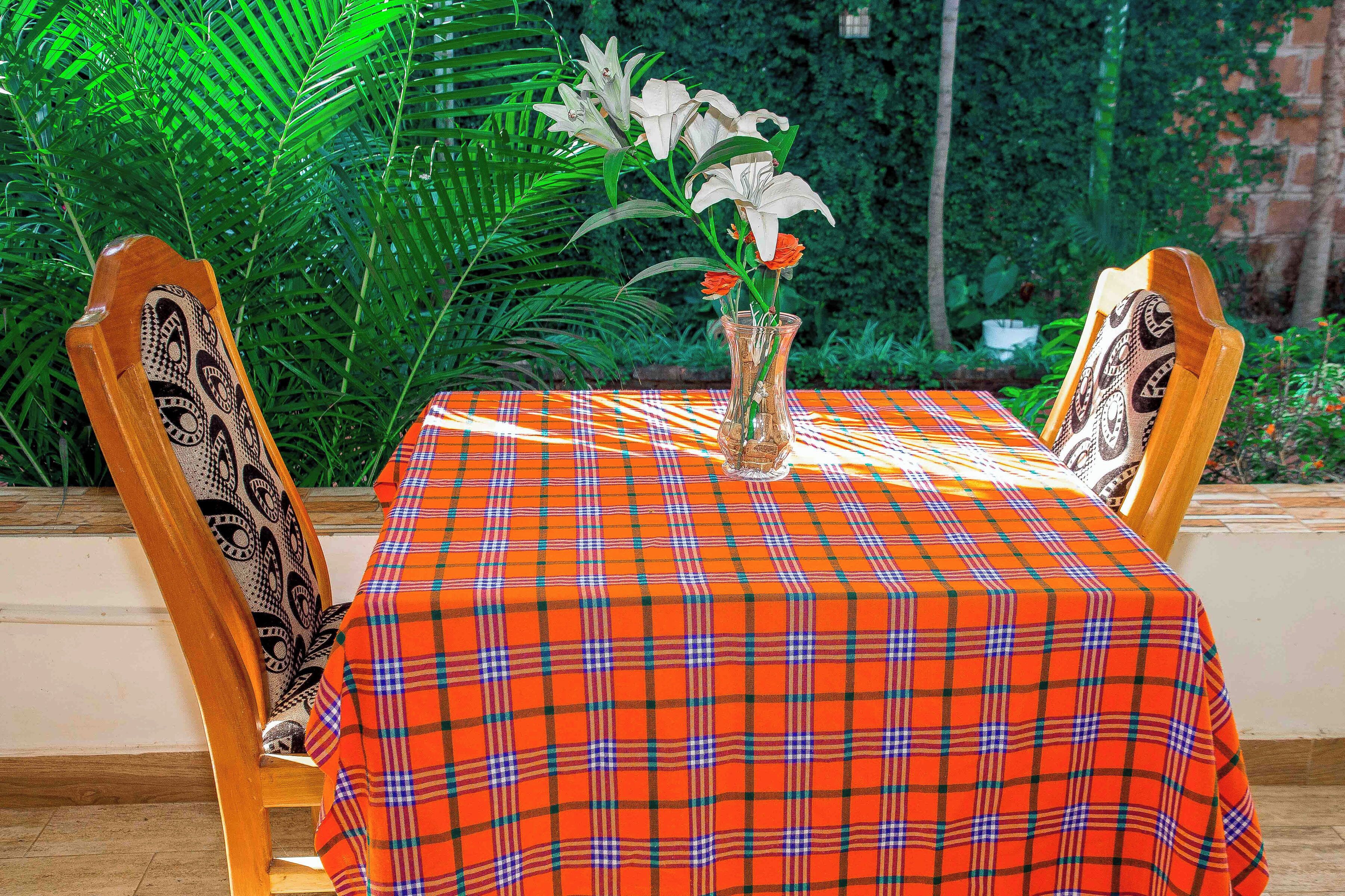 A table with a plaid tablecloth, two chairs with patterned upholstery, and a vase with flowers.