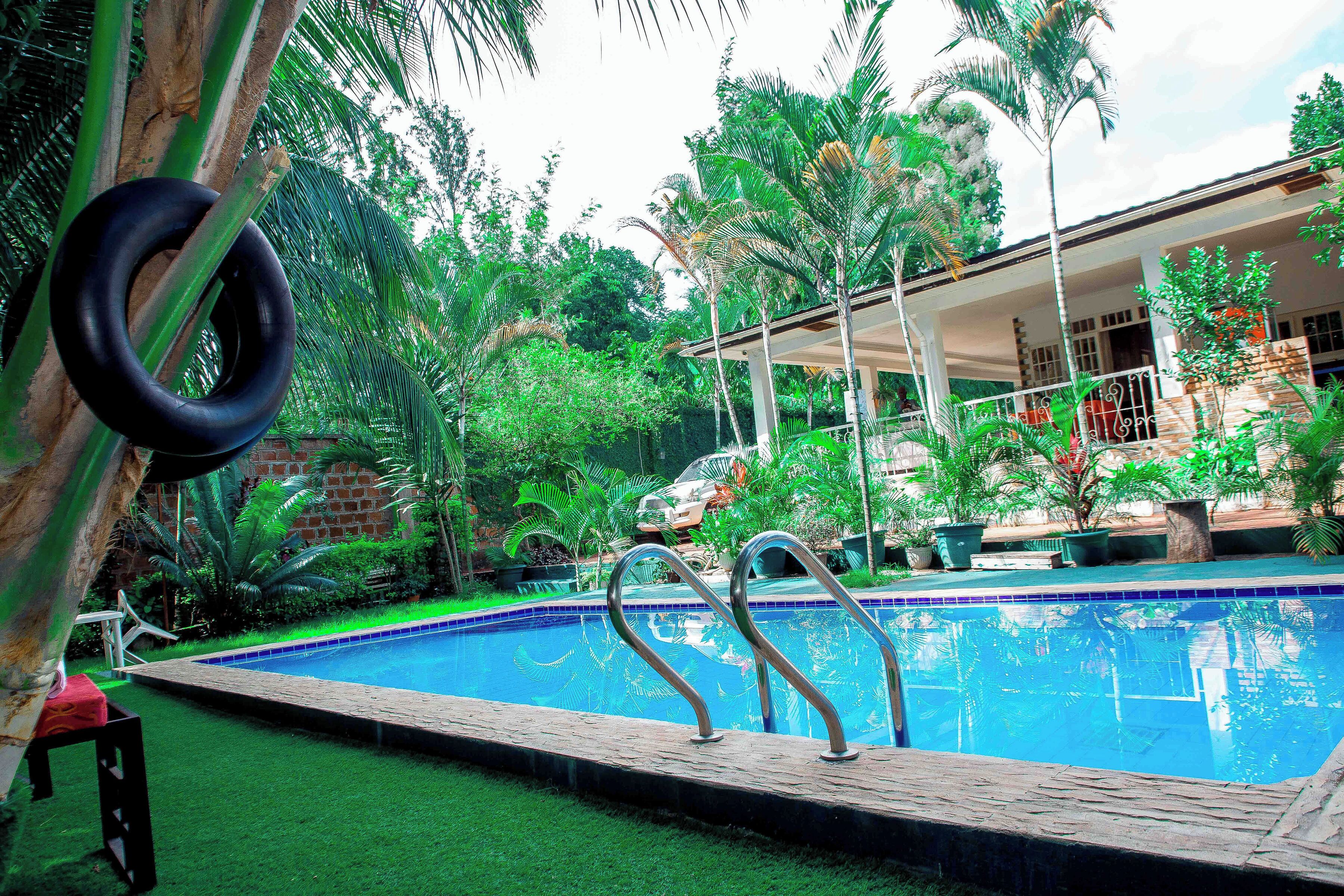 A swimming pool with metal railings, surrounded by lush greenery and a building with a covered patio.