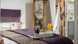 A bedroom with a bed, a bedside table with a tray of breakfast items, a mirror, and a view of the outdoors. - Lavender Cottage (Cheltenham)
