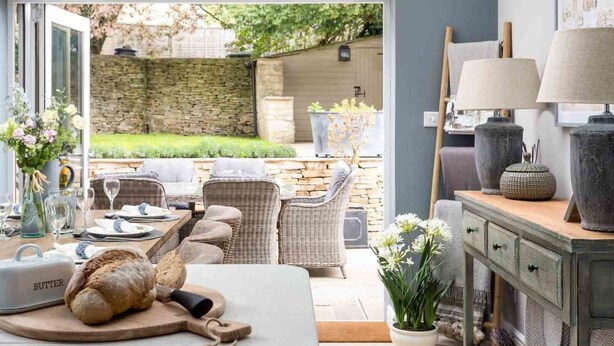 A cozy dining area with wicker furniture, a clock, and a view of the garden. - Lavender Cottage (Cheltenham)