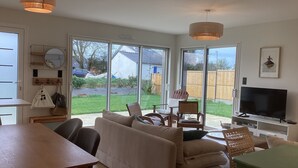 A spacious living room with a large TV, comfortable seating, and a view of the backyard through sliding glass doors.