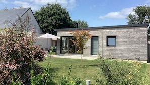 A modern building with a glass door entrance, a small patio area with outdoor seating, and a well-maintained lawn.