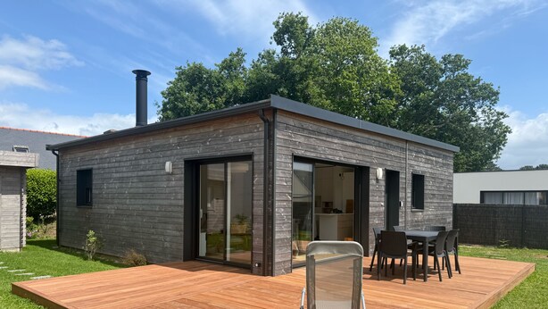 A modern house with a deck, a sliding glass door, and a chimney.