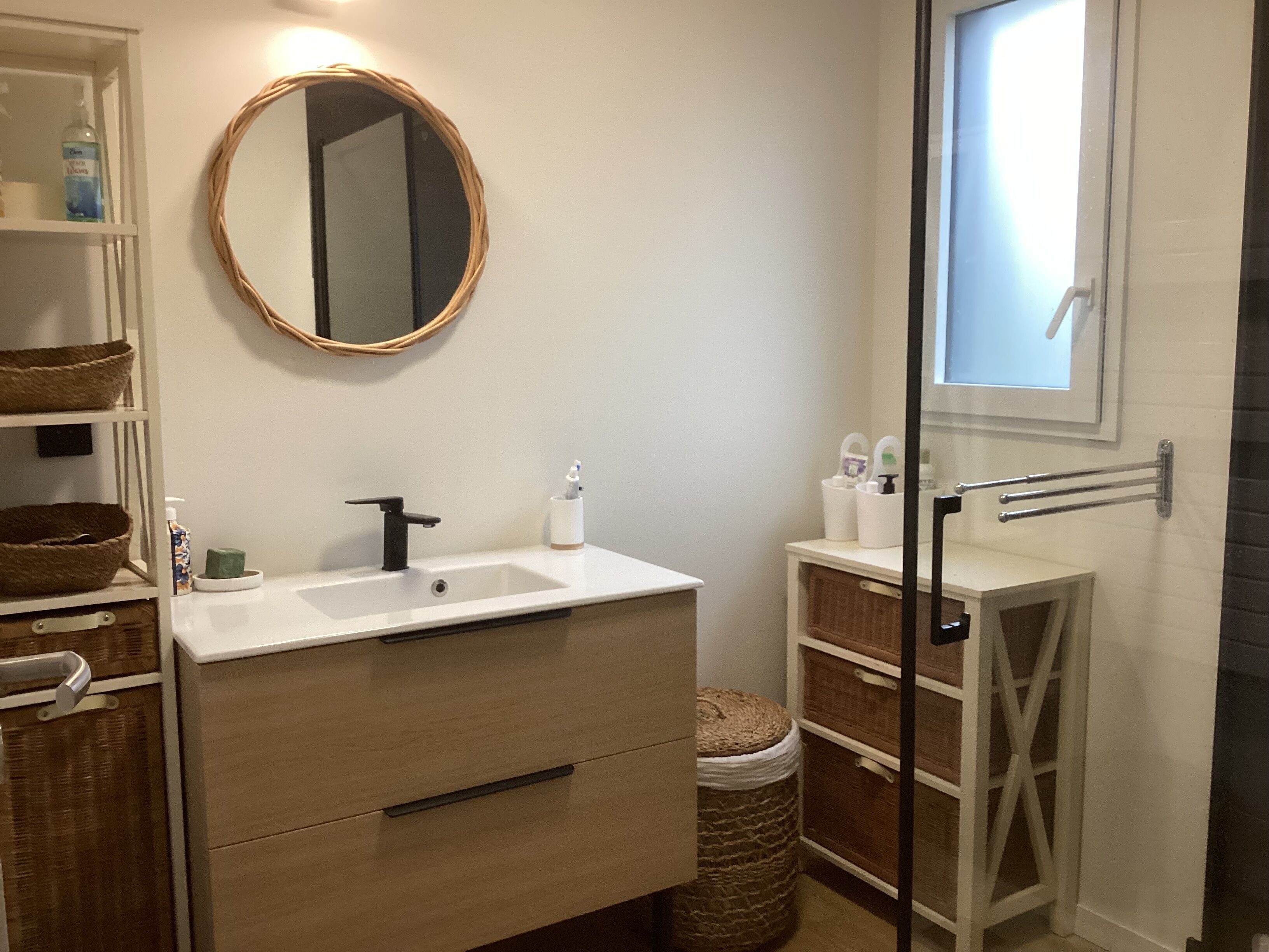 A bathroom with a white sink, wooden vanity, wicker baskets, and a round mirror.