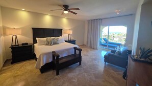 A hotel room with a bed, bedside tables, a ceiling fan, a balcony with a view of the ocean, and a seating area with a sofa and armchairs. - Las Mananitas Luxury Triple en-suite Ocean & Beach Front Resort Condo (San José del Cabo)