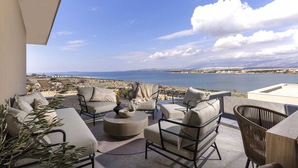 Une terrasse avec mobilier d’extérieur, une vue sur la mer et un paysage rocheux.