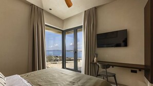 Une chambre avec un lit, un bureau, une chaise, une télévision et une vue sur la mer.
