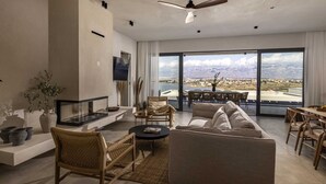 Un vaste salon comprenant un grand canapé, une table basse et un coin repas avec des chaises et une table. Une grande fenêtre offre une vue sur la ville et les montagnes.