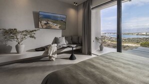 A modern bedroom with a large bed, a sofa, and a view of a coastal landscape. - Villa Salina with Pool (Povljana)