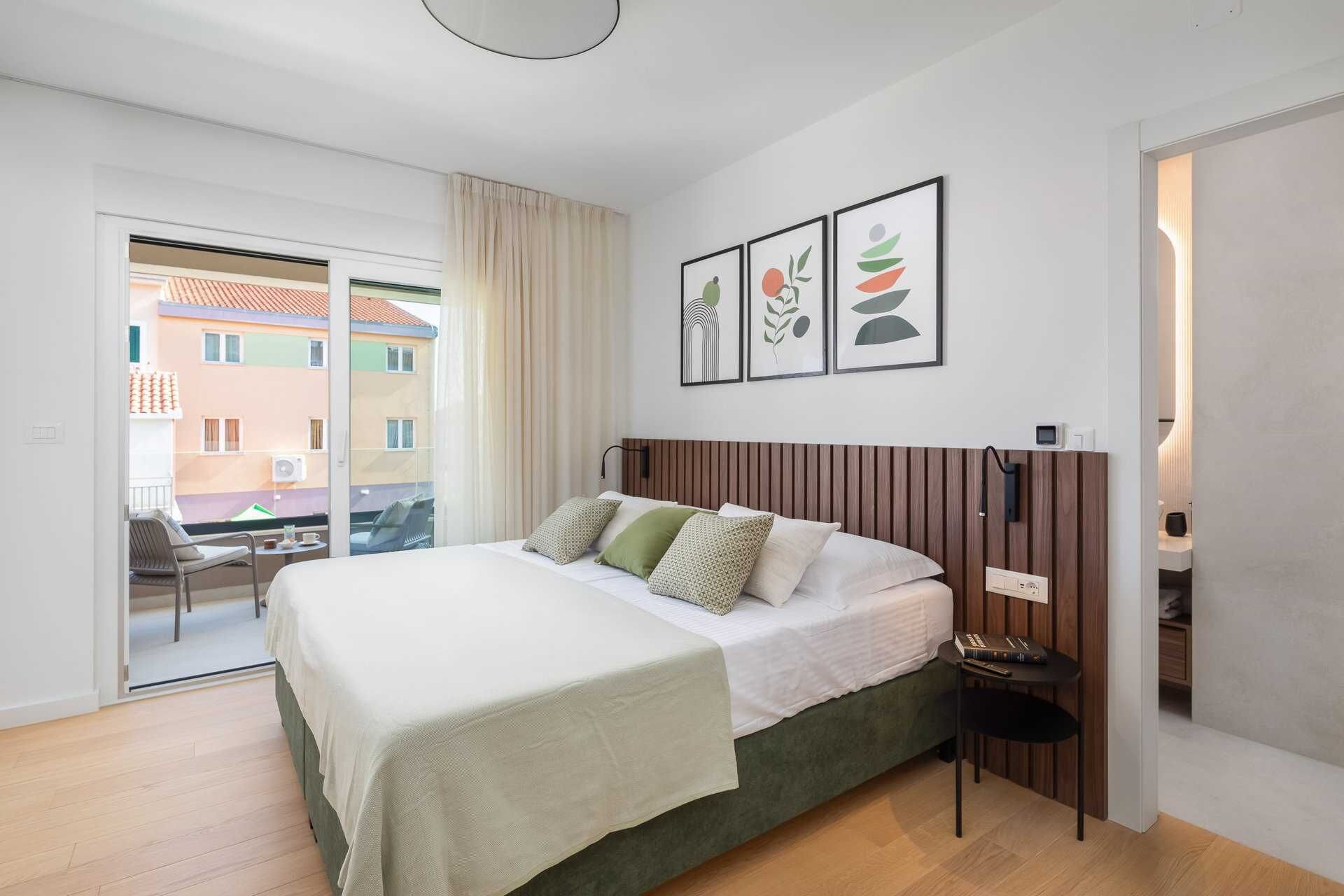 A modern bedroom with a bed, a bedside table, a chair, and a view of the outside.