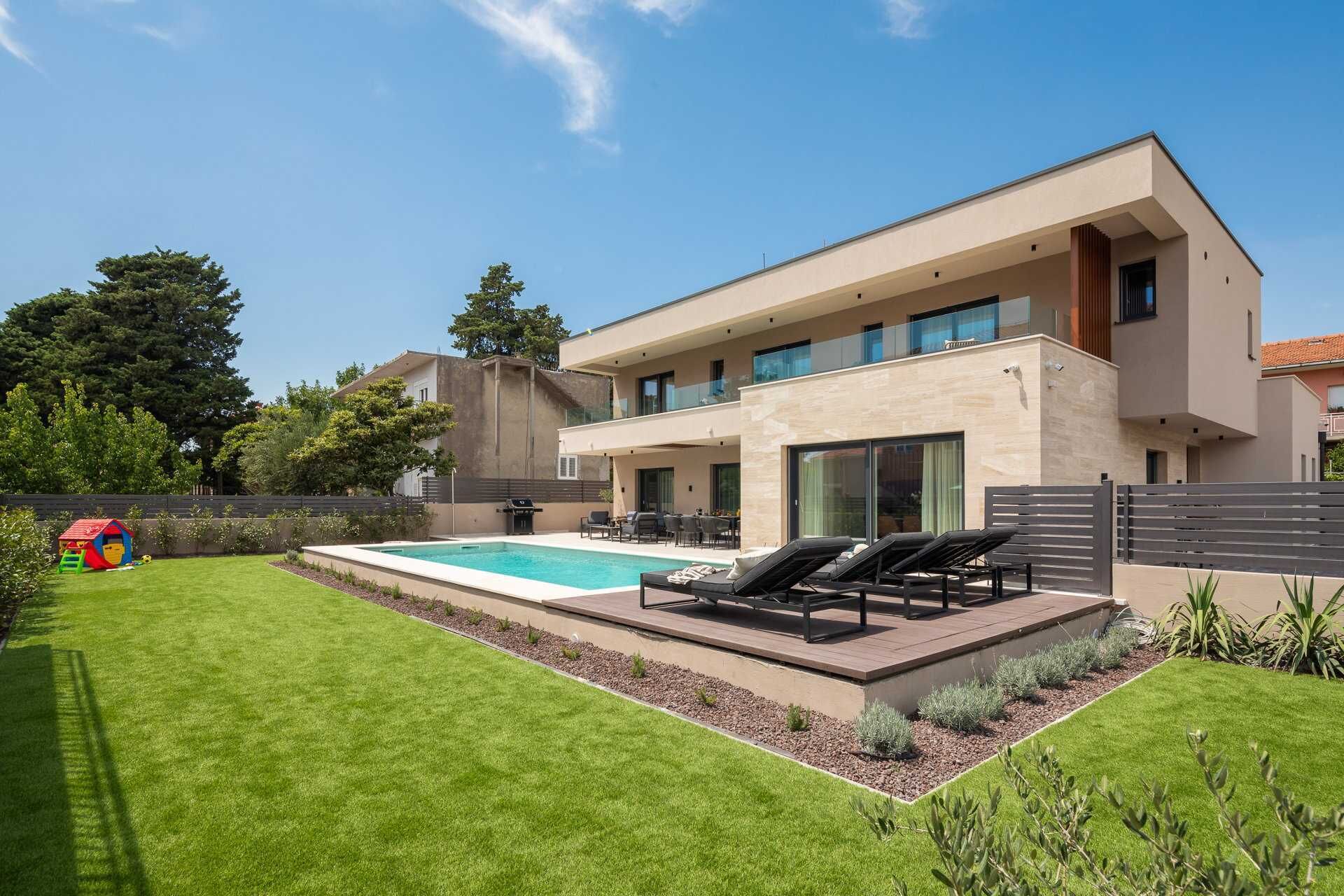 A modern two-story house with a swimming pool, outdoor seating, and a well-maintained lawn.
