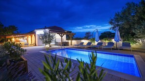 A swimming pool with lounge chairs and umbrellas, a barbecue area, and a building with a sign. - Villa Aquaterra with pool (Nin)
