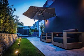 Een terras buiten, modern ingericht, met een grote parasol, zitplaatsen en een verzorgd gazon.