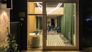 Entrada de un hotel con puerta de vidrio, un jarrón grande y piso estampado.