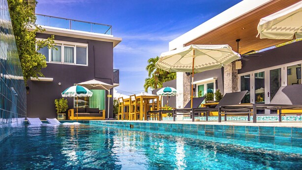 Una piscina con sillas de descanso y sombrillas, rodeada de edificios modernos con ventanas amplias y balcones.