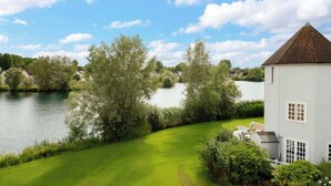 A white building with a conical roof near a lake, surrounded by greenery and trees.