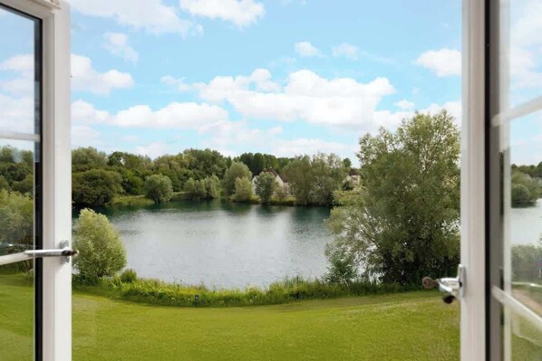 A view through an open door of a lake surrounded by greenery and trees.
