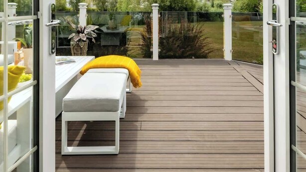 An open deck with a white bench and a yellow towel, overlooking a garden and a lake.