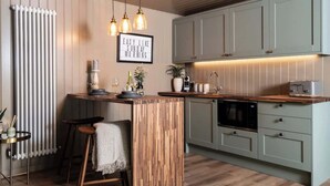 A modern kitchen with a wooden island, bar stools, a hanging light fixture, and a framed quote on the wall. - Rabbits Warren - Cotswolds Stay with Sauna and Hot Tub (Wiltshire)