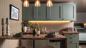 A kitchen with a wooden island, green cabinets, pendant lights, and a framed sign on the wall. - Rabbits Warren - Cotswolds Stay with Sauna and Hot Tub (Wiltshire)