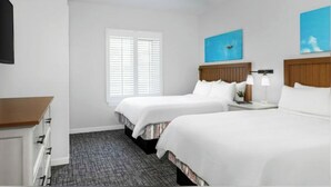 Une chambre d’hôtel avec deux lits, un ventilateur de plafond, une fenêtre avec des stores et des œuvres d’art accrochées aux murs.