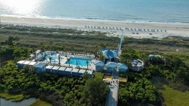 Vue aérienne d’un complexe hôtelier avec une piscine, des parasols de plage et une plage.