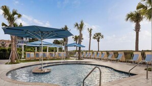 Une piscine entourée de palmiers, avec des chaises longues et des parasols.