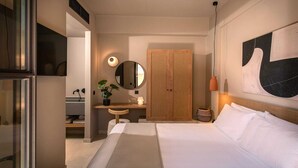 Ein Hotelzimmer mit einem Bett, einem Holzschrank, einem runden Spiegel, einem kleinen Schreibtisch mit Lampe und einer Zimmerpflanze.
