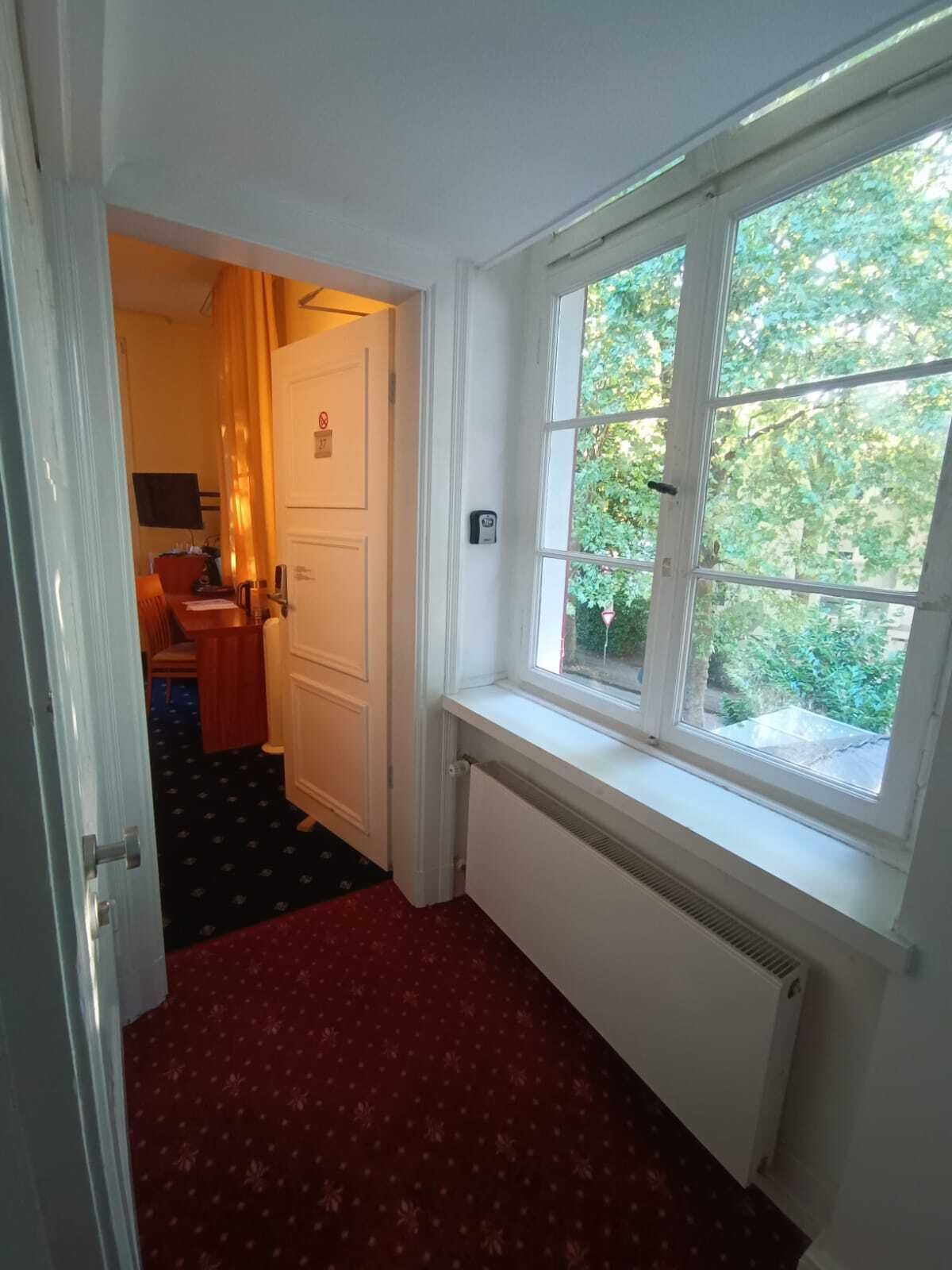 Een kamer met een raam, radiator en een deur naar een andere kamer.