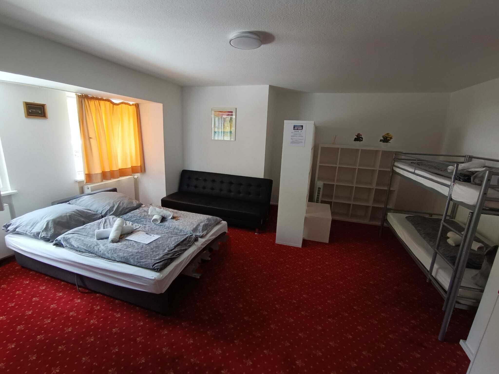 A small, compact room with a bed, a sofa, a bunk bed, and a small window with curtains.