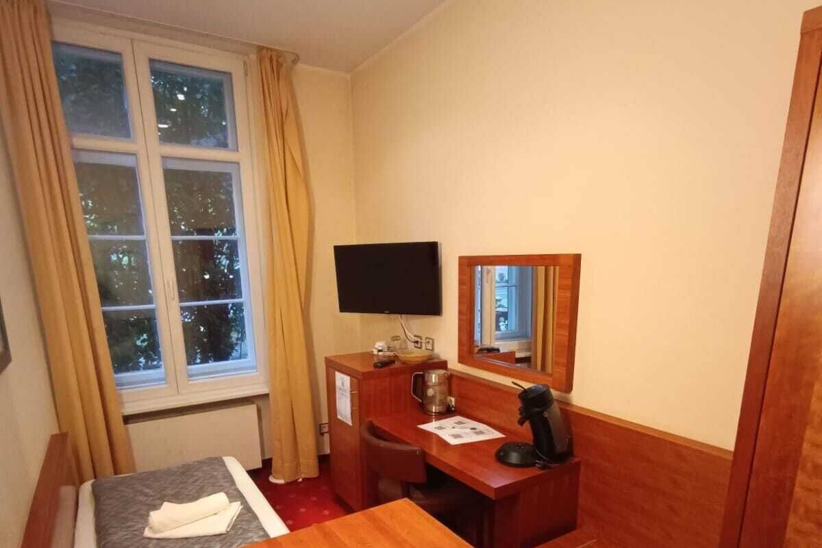 Ein Hotelzimmer mit Bett, Schreibtisch, Sessel, Fernseher und einem fenster mit Vorhängen.