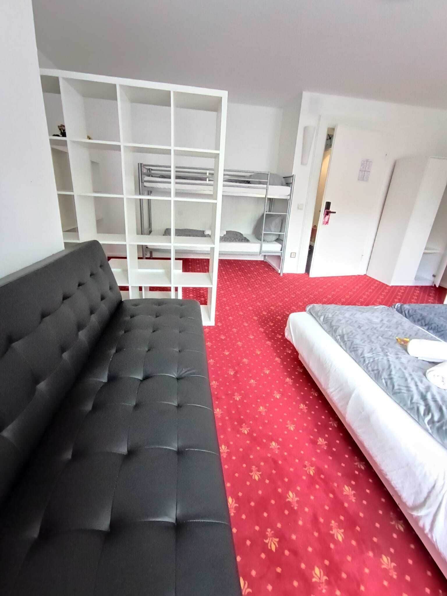 Una habitación con un sofá negro, una cama con colchón gris y un estante blanco.