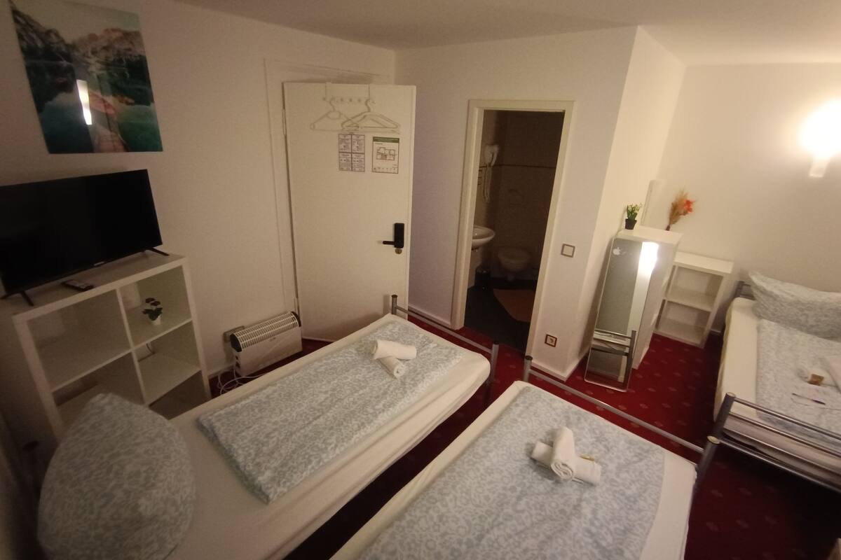 Ein Hotelzimmer mit zwei Betten, einem Fernseher, einem Schreibtisch und einem durch eine offene Tür einsehbaren Badezimmer.