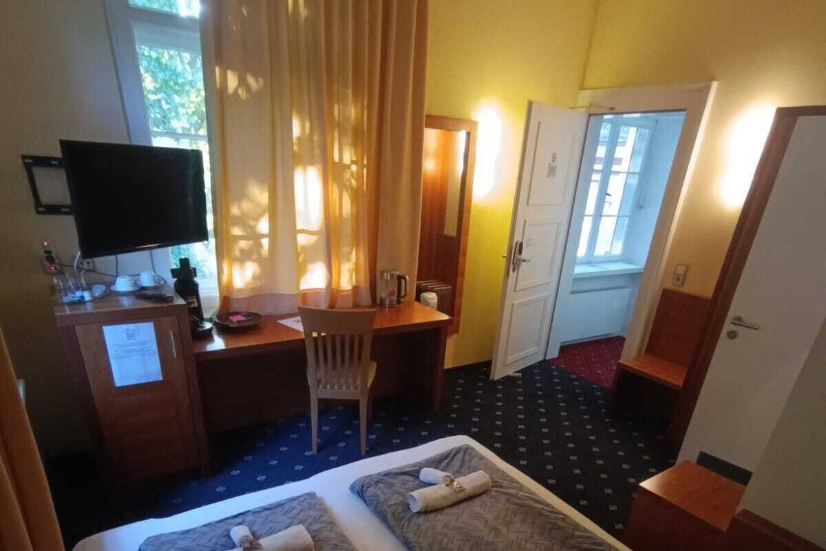 Ein Hotelzimmer mit zwei Betten, einem Schreibtisch, einem Sessel, einem Fernseher und einer Tür.