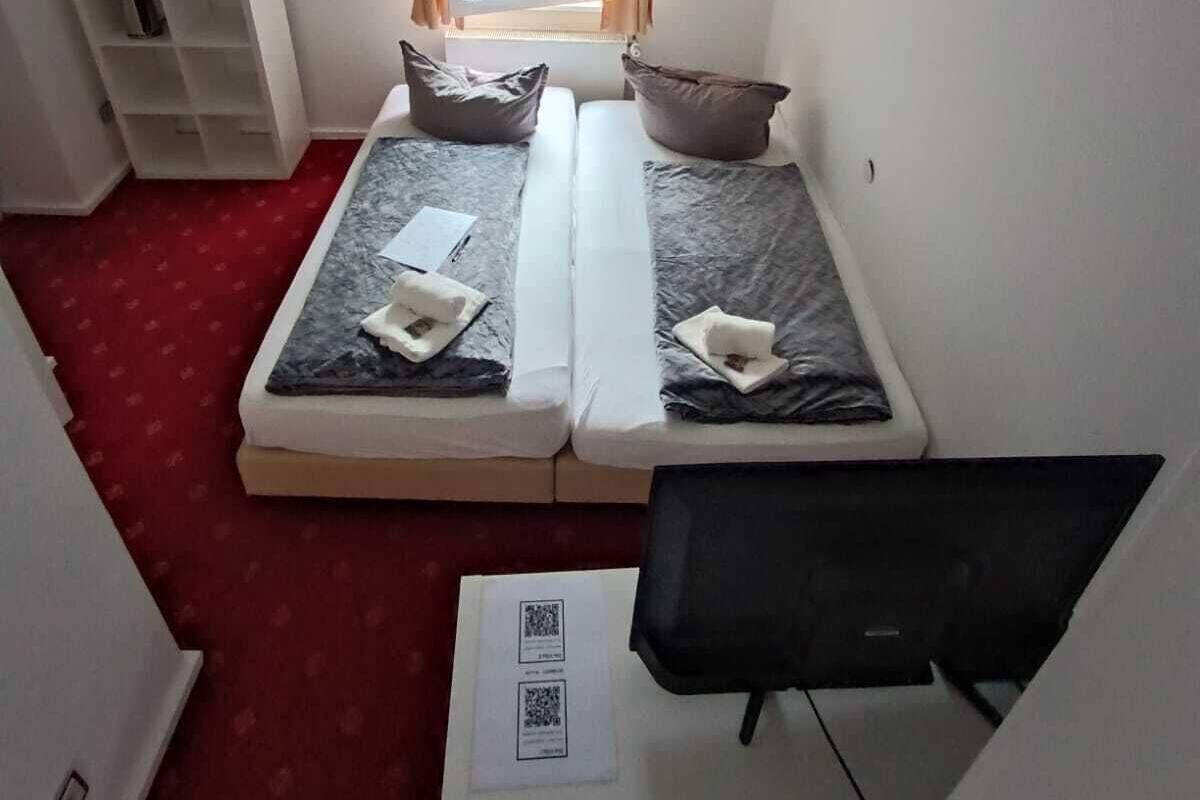 Ein kleines Zimmer mit einem Einzelbett, einem Fenster, einem Schreibtisch und einem Stuhl.