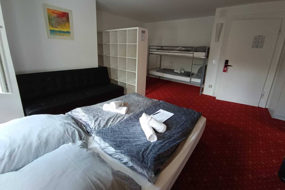 Ein Hotelzimmer mit einem Bett, einer schwarzen Couch, einem Stockbett und einem roten Teppich.