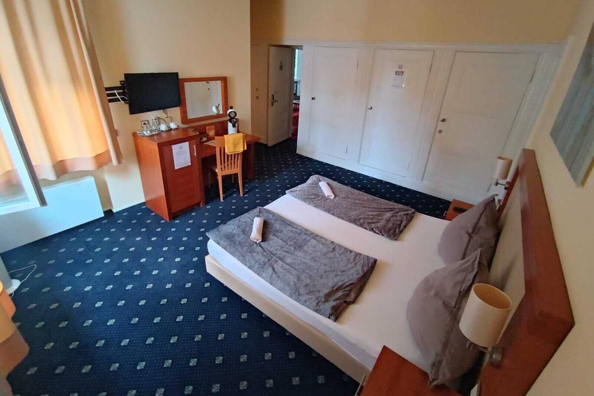 Ein Hotelzimmer mit Bett, Schreibtisch, Sessel, Fernseher und Kleiderschrank.
