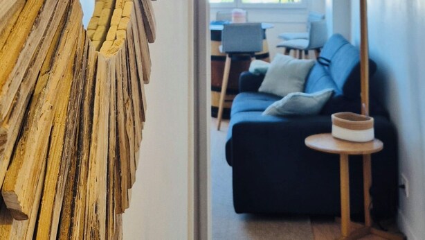 A hallway with a wooden wall art piece, a dark sofa, and a floor lamp.