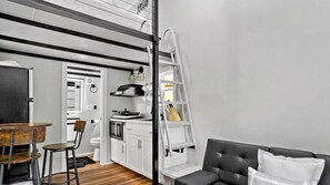 A compact living space with a dining area, kitchenette, and a black leather sofa.