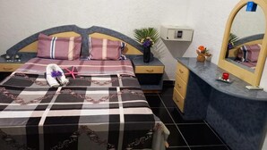 A bedroom with a checkered bedspread, a nightstand with a vase of flowers, a dresser with a mirror, and a small plant on the dresser.