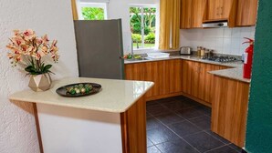 A compact kitchen with wooden cabinets, a stainless steel refrigerator, and a small countertop with a vase of flowers.