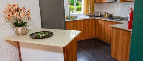 A compact kitchen with wooden cabinets, a stainless steel refrigerator, and a small countertop with a vase of flowers.