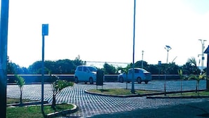 A parking area with two cars, a paved walkway, and street lamps.