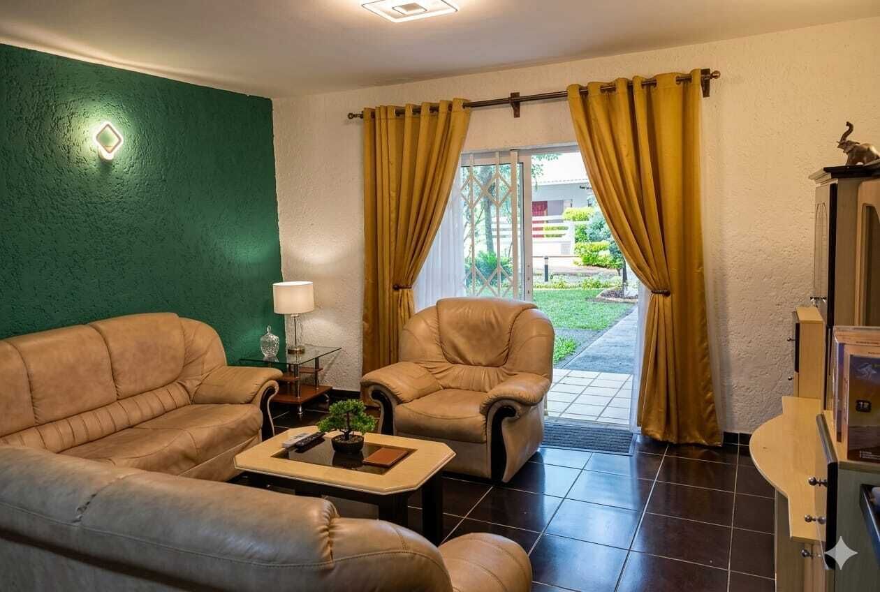 A room with a sofa, armchair, and a small table with a lamp and a plant.