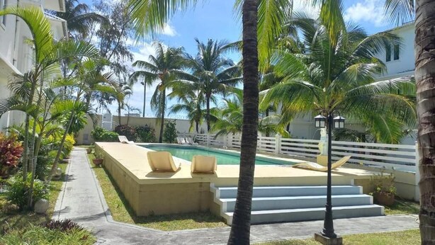 A pool area with lounge chairs, palm trees, and a staircase leading to a building.
