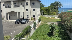 A multi-story building with a parking lot, a grassy area, and a view of the ocean.