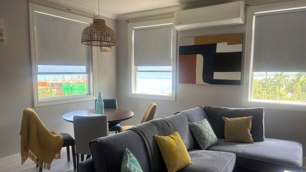 A modern living room with a grey sectional sofa, a dining table, and a hanging light fixture.