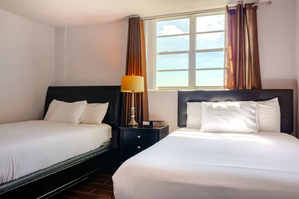 Una habitación de hotel con dos camas, una mesita de noche con lámpara y una ventana con cortinas.