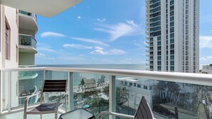 A balcony with a glass railing, two chairs, and a table. - The Tides (Hollywood)