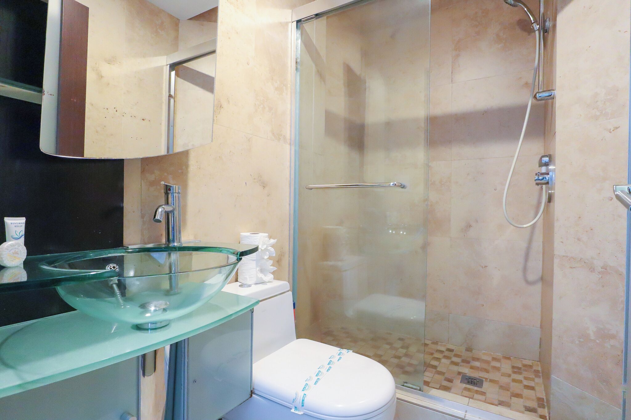 Un baño con lavamanos de vidrio, inodoro y zona de ducha con mampara de cristal.